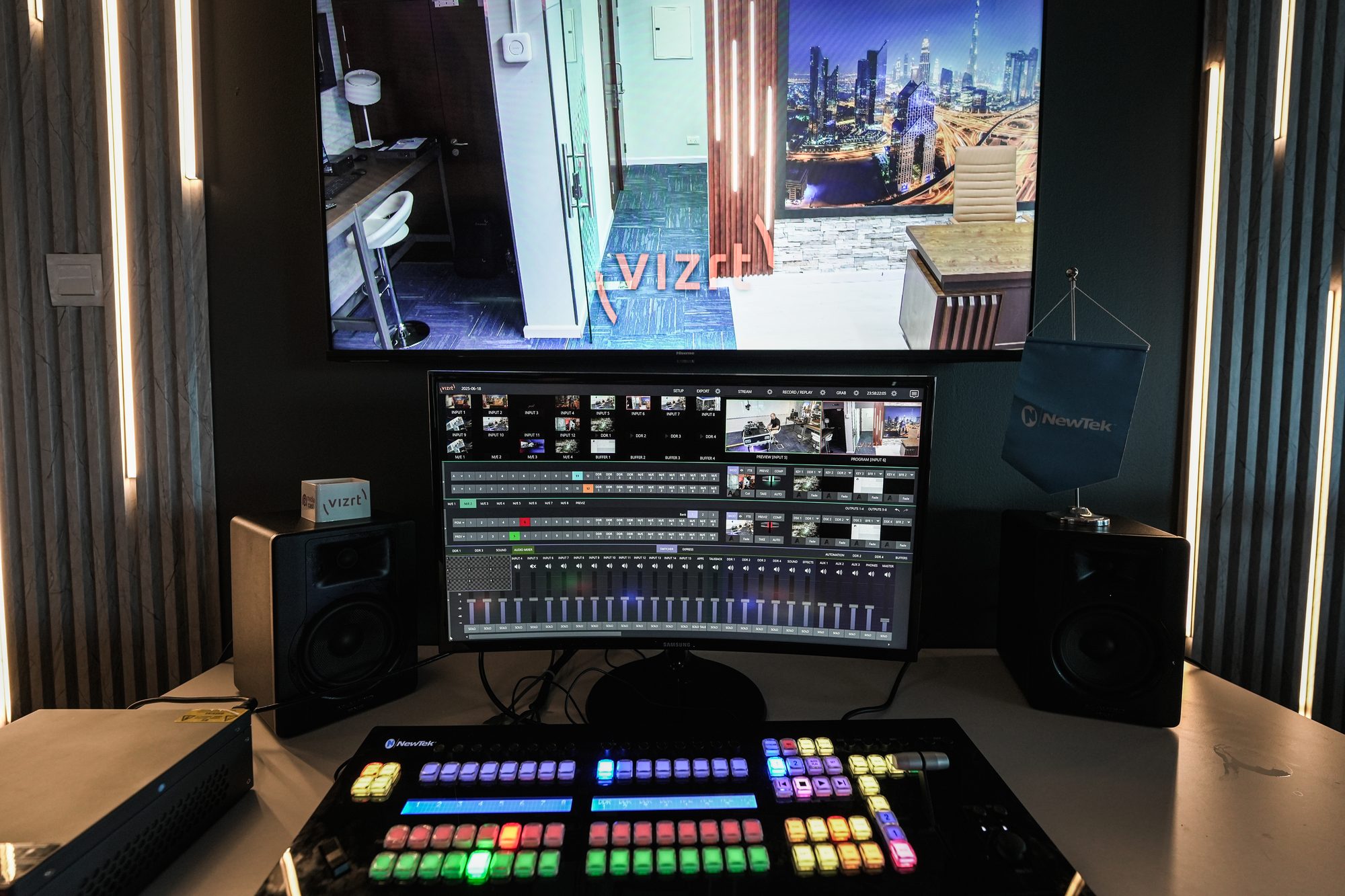 A production gallery desk, switcher keys lit in colour beneath the programme screens
